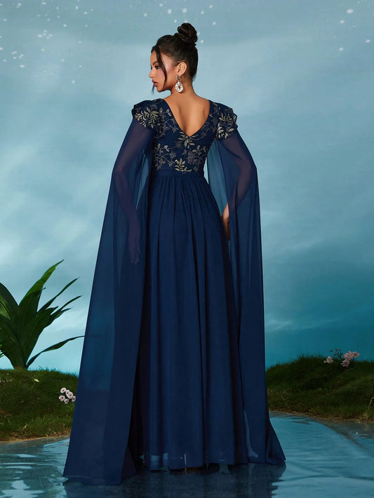 Woman in a long blue dress with a cape standing on a reflective surface with a blurred natural background