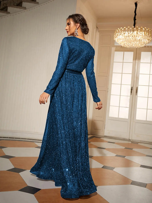 Woman in a blue sparkly dress standing in an elegant room with chandelier.