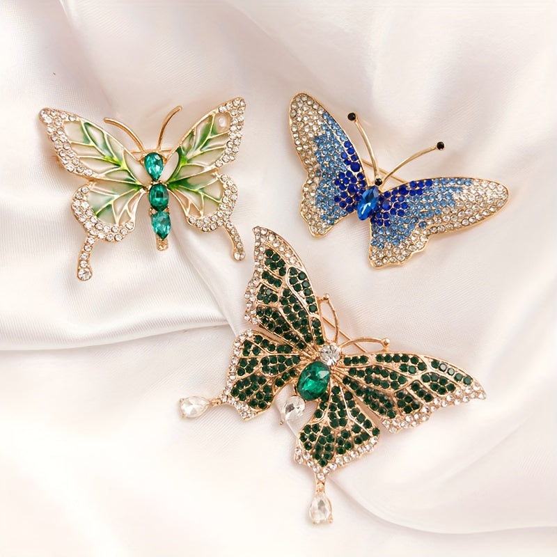 Three butterfly-shaped brooches with gemstones on a white fabric background