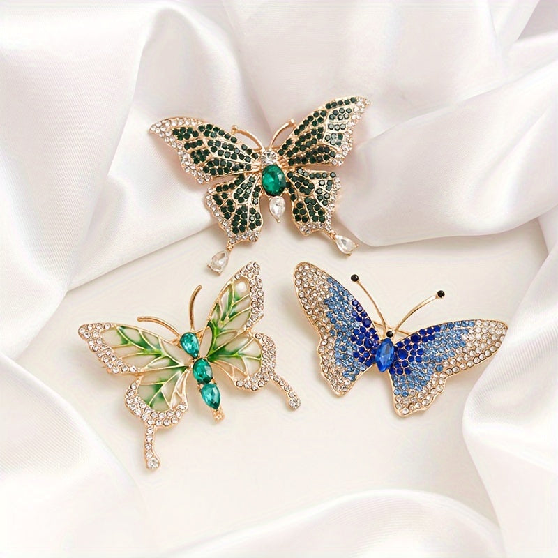 Three butterfly-shaped brooches with gemstones on a white fabric background