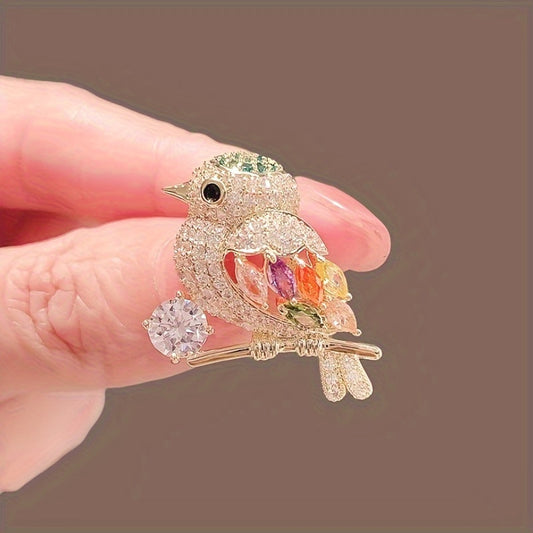 Decorative bird brooch with gemstones held between fingers against a brown background