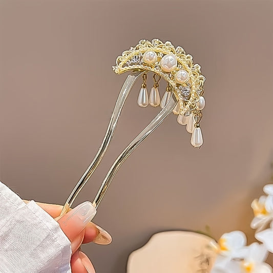 Decorative hairpin with pearls and gold details held by a hand against a neutral background