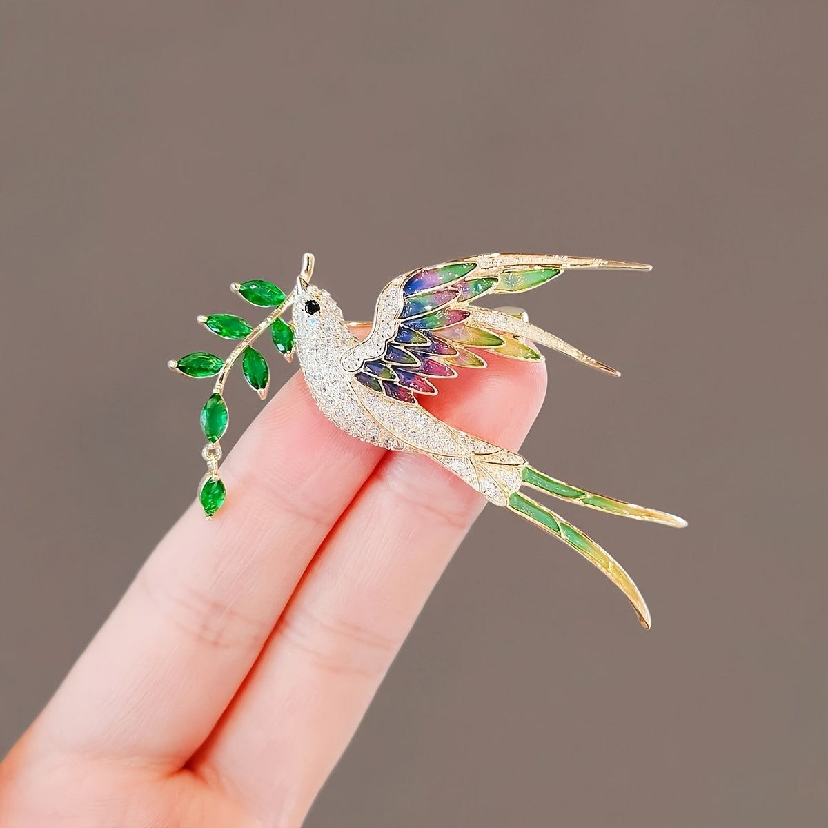 Delicate bird-shaped brooch with gemstones held by a hand against a neutral background