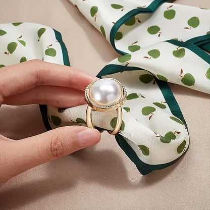 Gold ring with a pearl held over a patterned fabric background