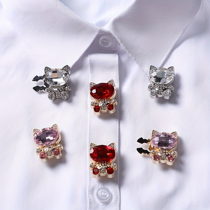 Five cat-shaped jewelry pins with gemstones on a white shirt background