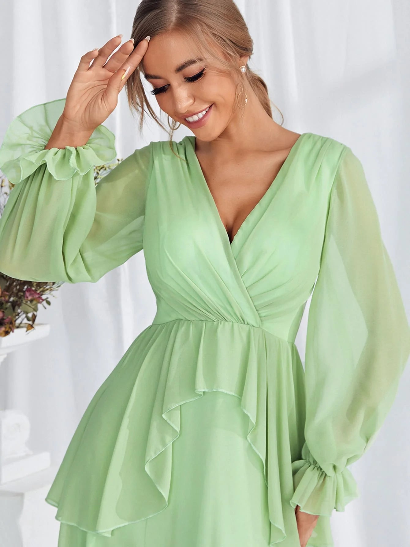 Woman wearing a light green dress with long sleeves against a white background
