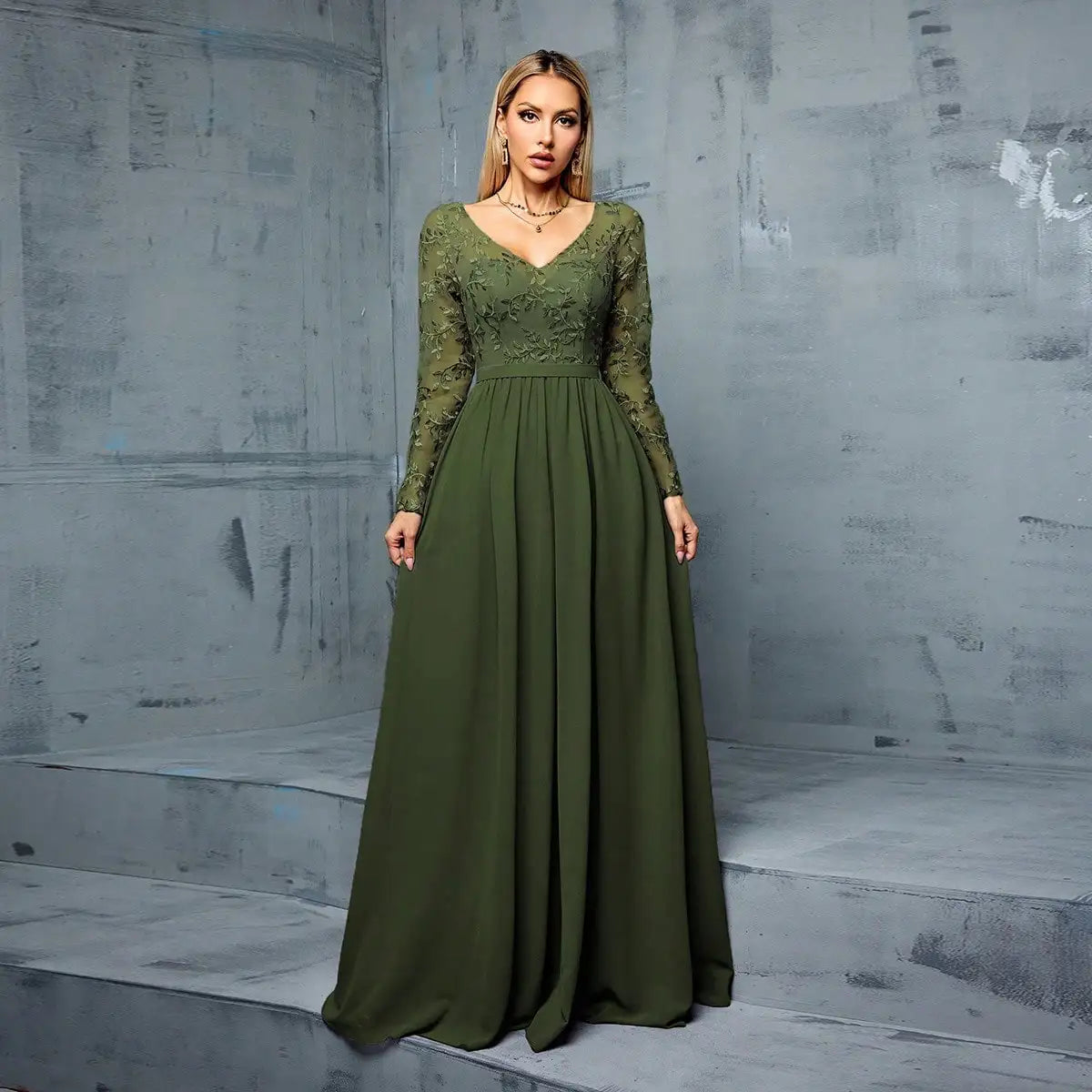 Woman wearing a green evening gown against a gray concrete wall.