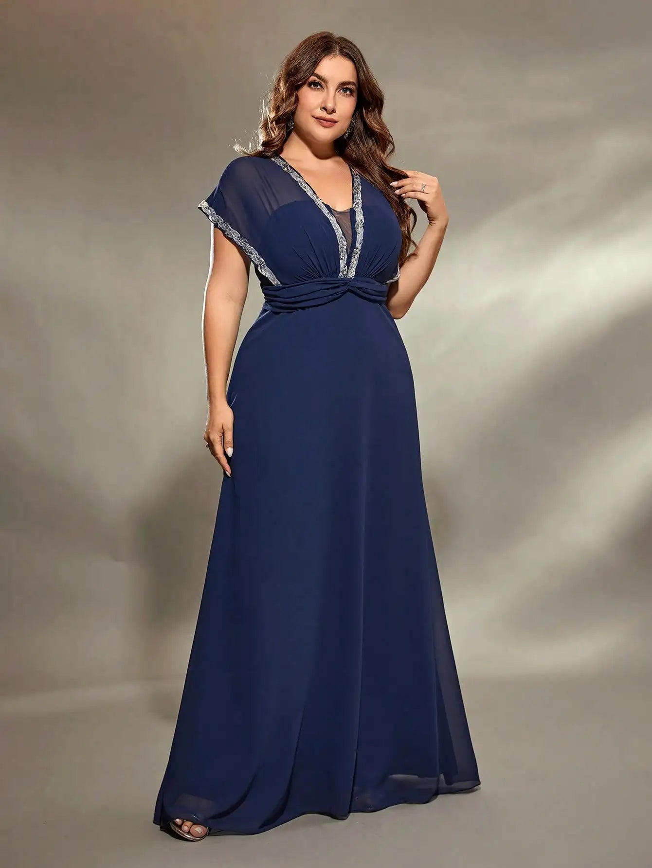 Woman wearing a navy blue evening gown with sheer sleeves against a neutral background