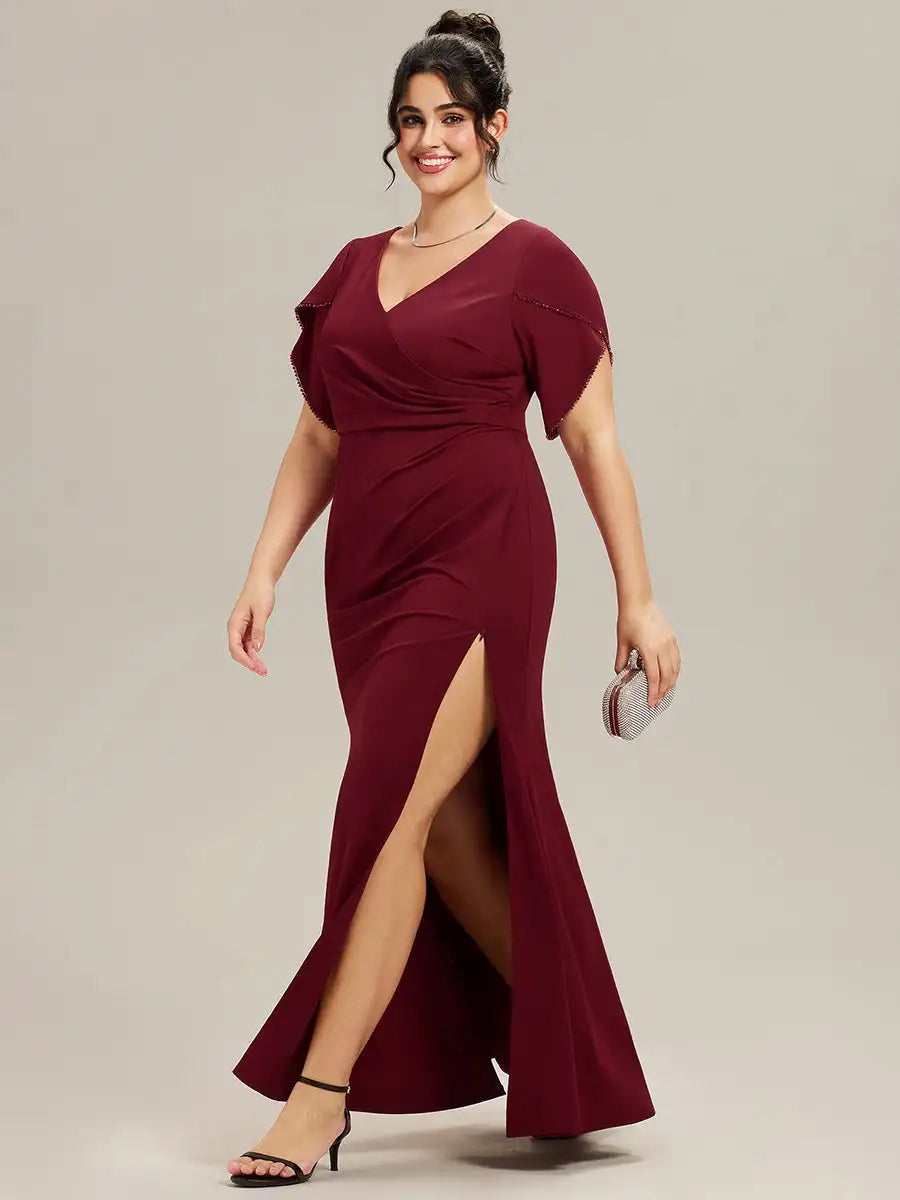 Woman wearing a burgundy evening gown with a slit on a plain background