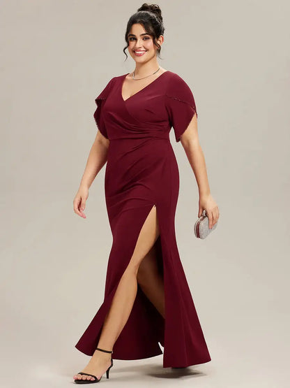 Woman wearing a burgundy evening gown with a slit on a plain background