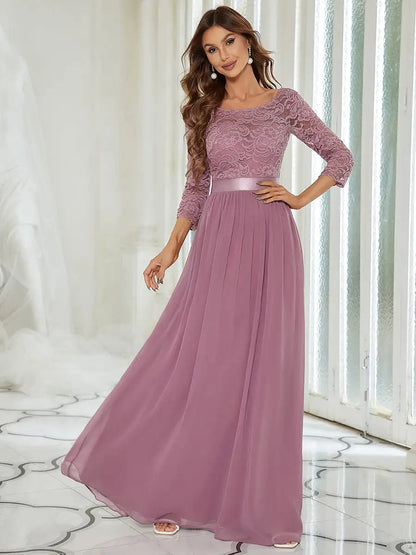 Woman wearing a long, elegant purple dress with lace top in a bright room.