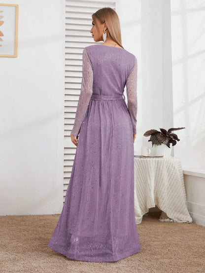 Woman wearing a long purple dress standing in a room with a white wall and a table with a plant.