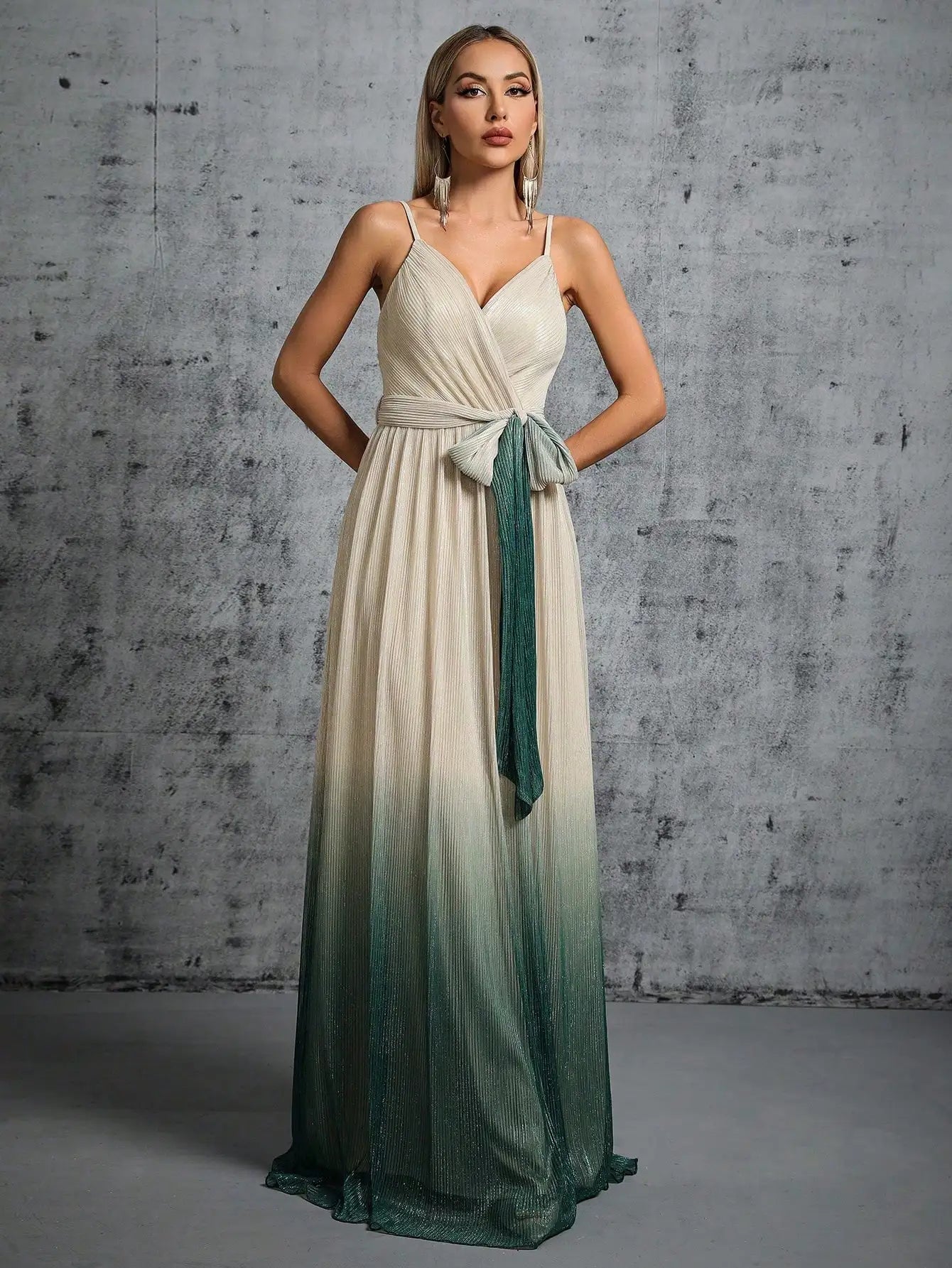 Woman wearing a long, gradient dress with a white top and green skirt against a gray concrete wall.