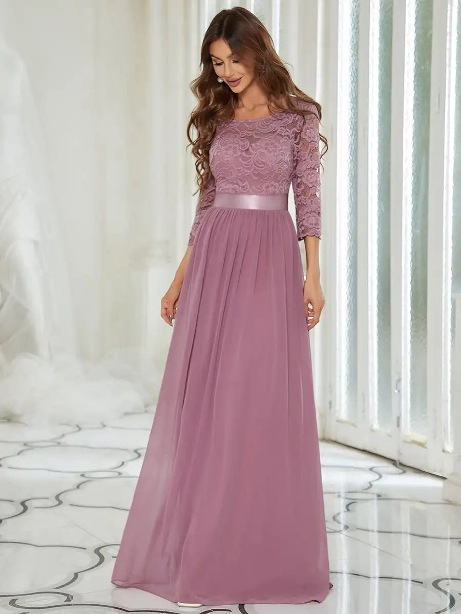 Woman wearing a long, elegant purple dress with lace detailing in a softly lit room.