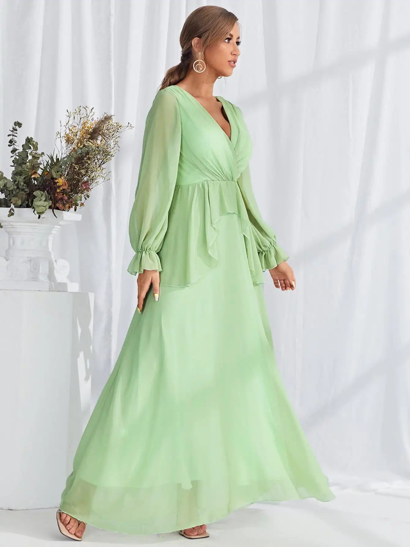 Woman wearing a light green dress with long sleeves against a white background