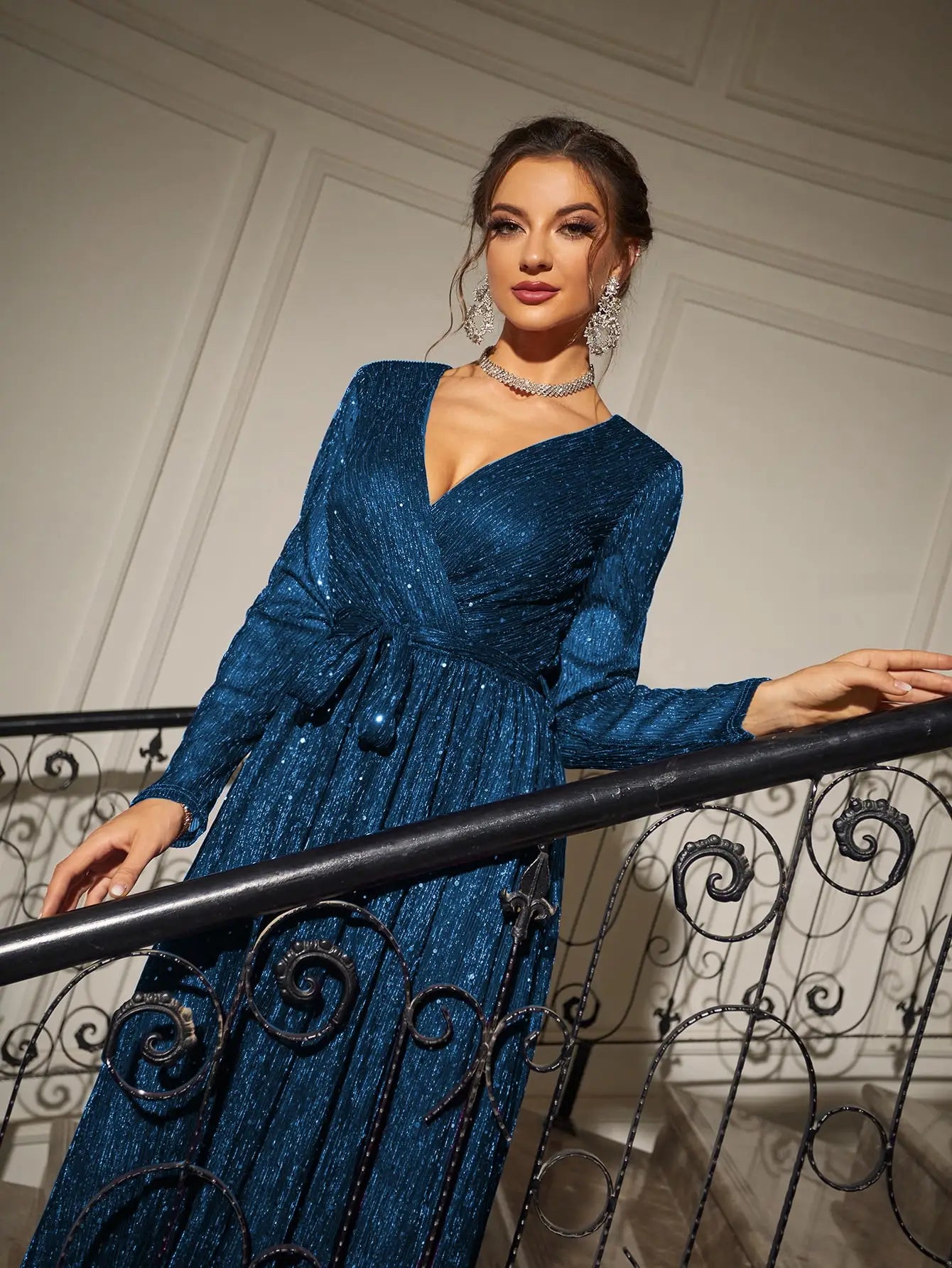 Woman in a blue dress standing on a staircase with white walls and decorative railings.