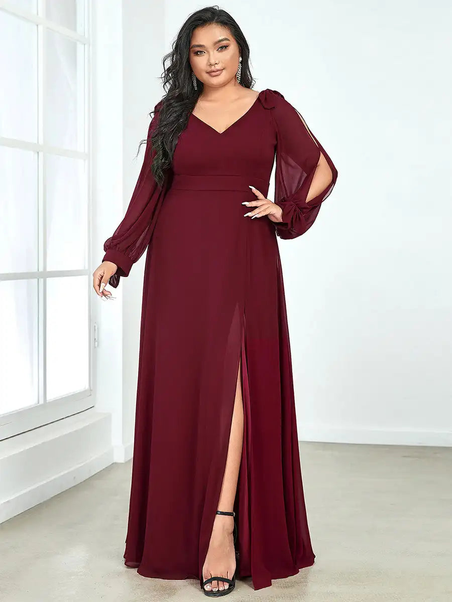 Woman wearing a burgundy evening gown with long sleeves and a slit skirt in a room with a window.