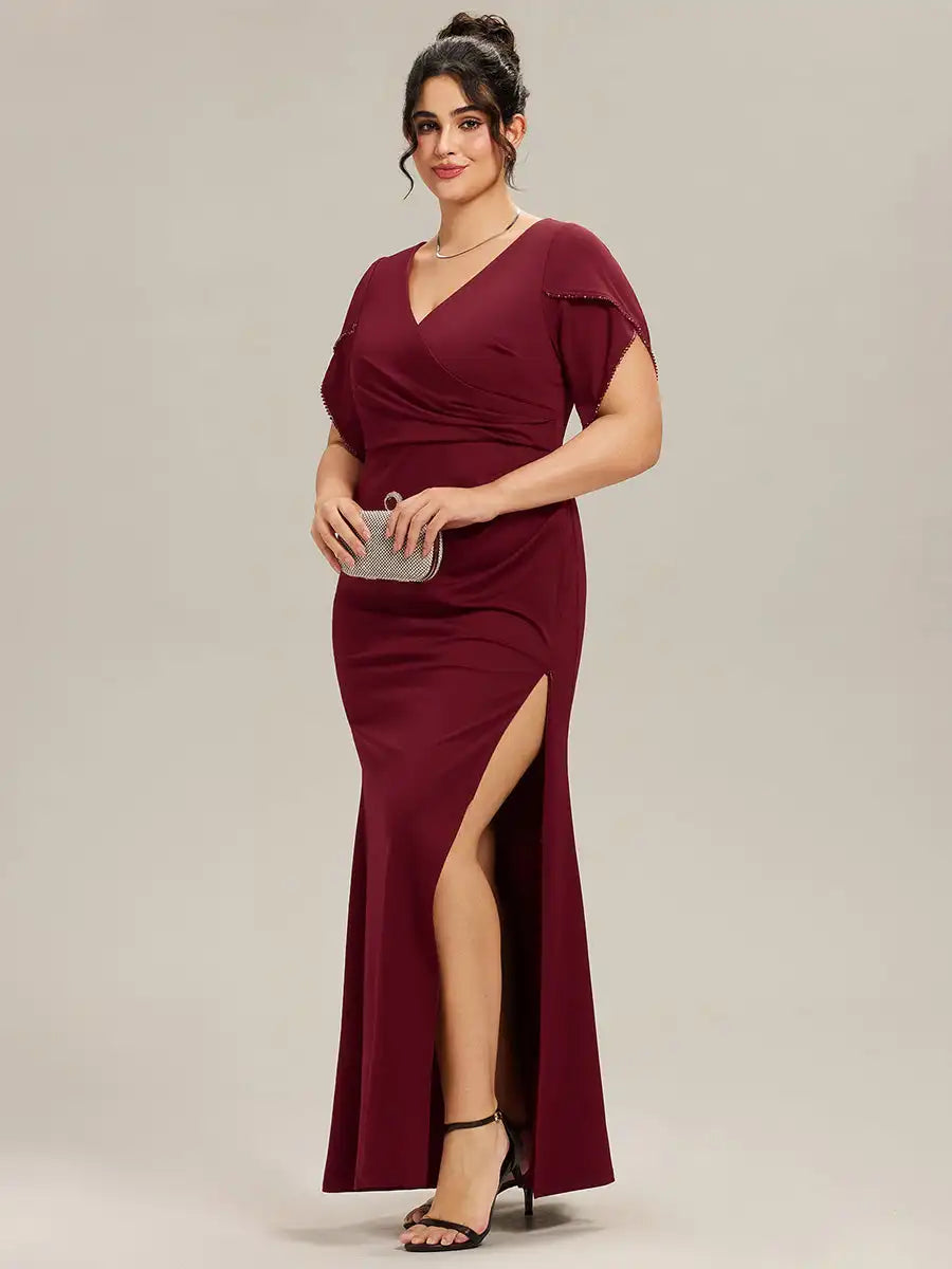 Woman wearing a burgundy evening gown with a slit on a plain background