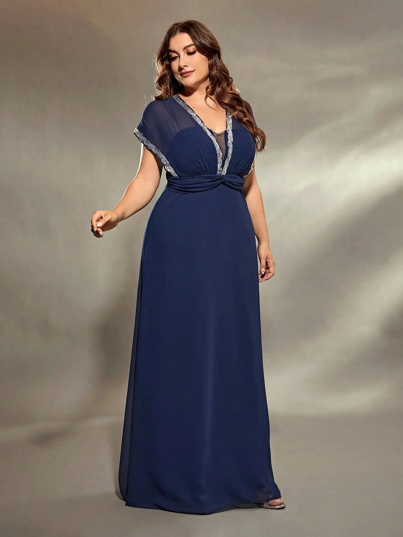 Woman wearing a navy blue evening gown with a gray trim against a neutral background