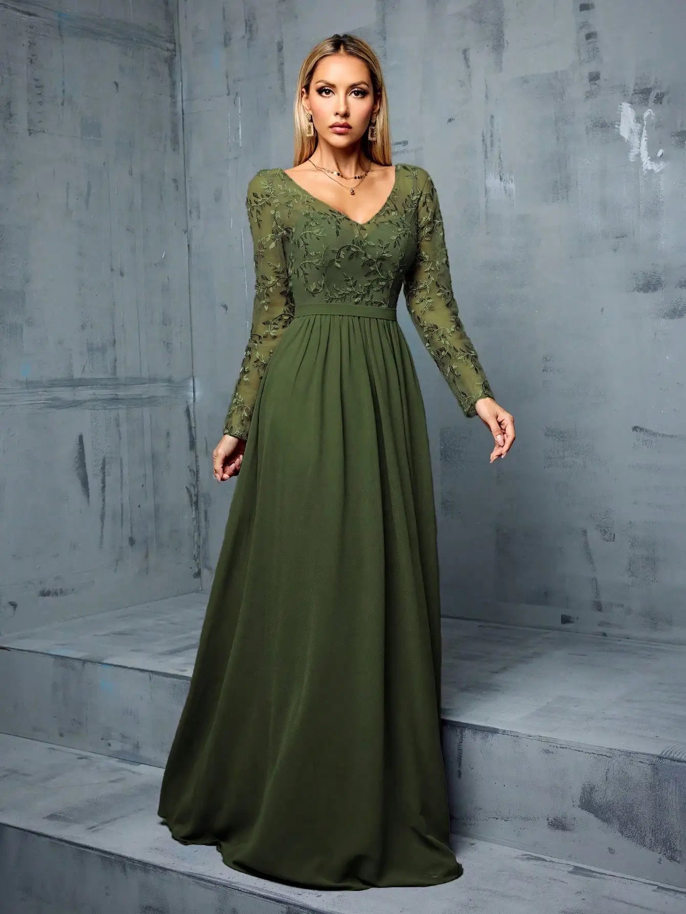 Woman wearing a green lace dress against a gray concrete wall.