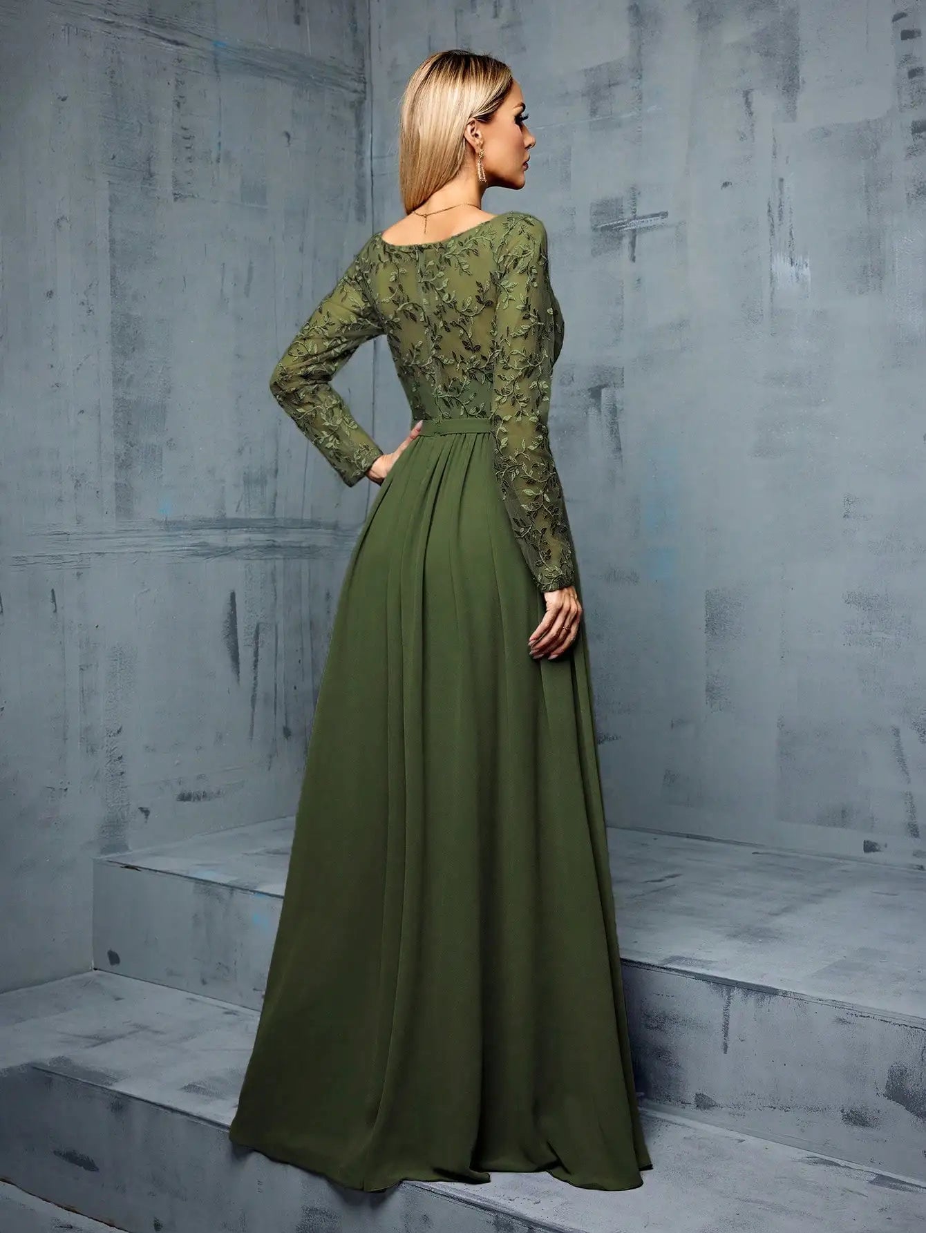 Woman wearing a green lace dress against a gray textured wall.