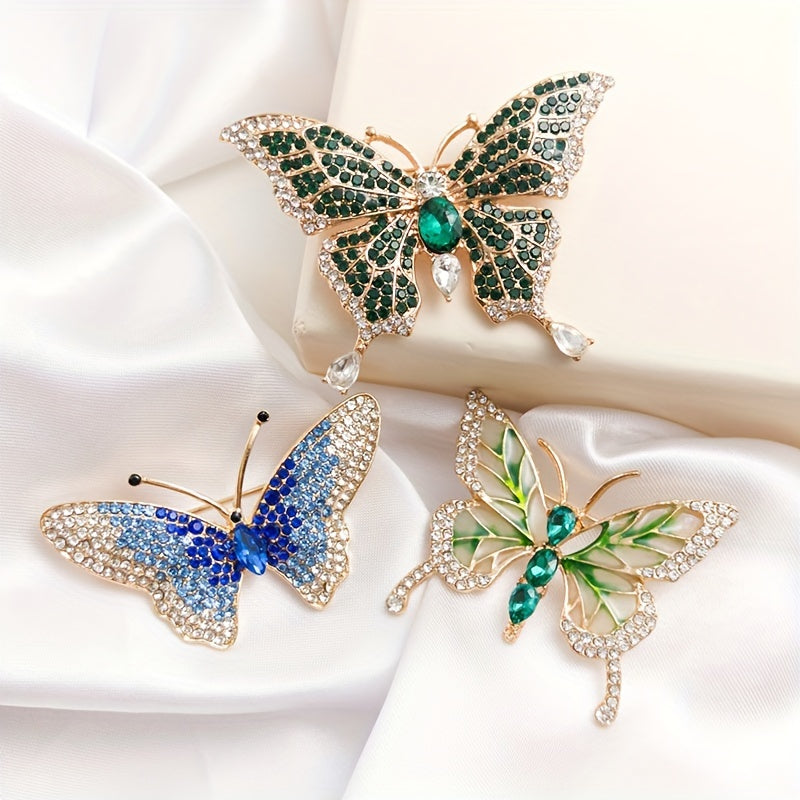 Three butterfly-shaped brooches with gemstone details on a white fabric background
